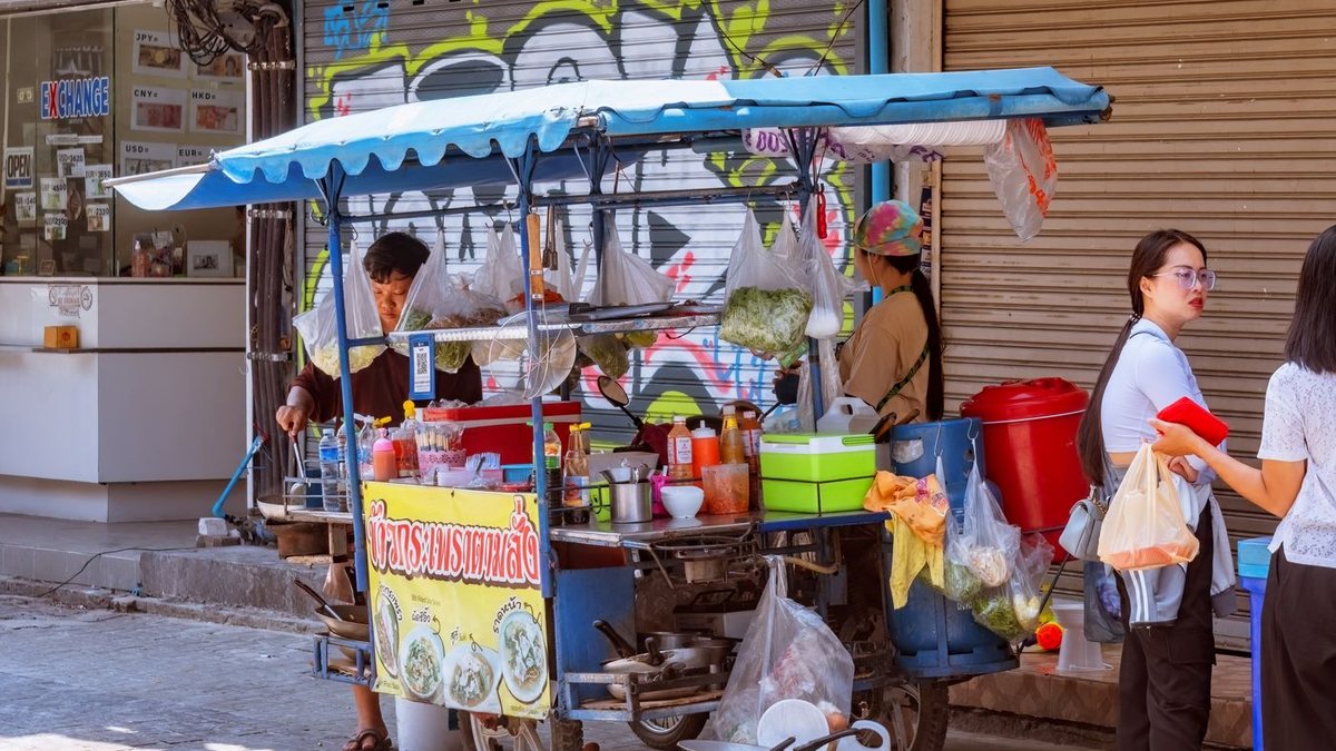 รถเข็นขายอาหารตามสั่งริมถนนในไทย มีลูกค้ายืนรอ
