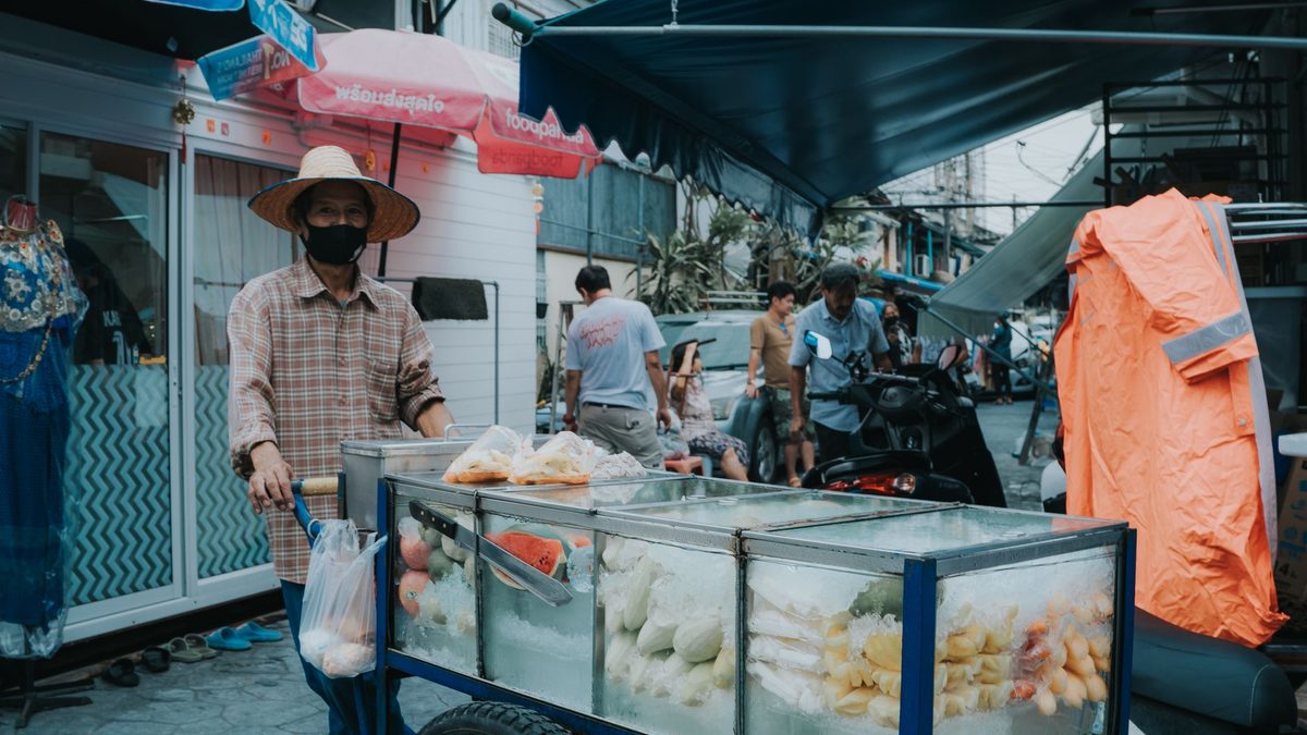 พ่อค้าเข็นรถขายอาหารในตลาดกลางแจ้ง มีลูกค้าเดินผ่านไปมา